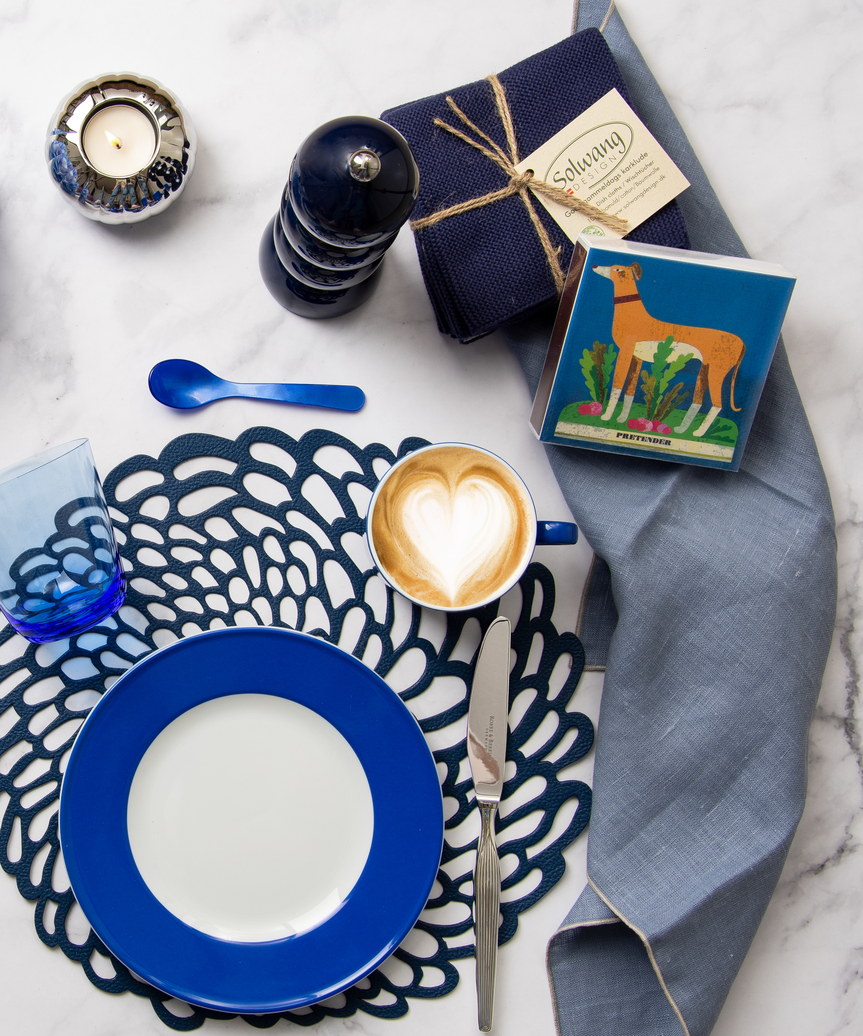 Ein gedeckter Marmortisch von oben fotografiert. Auf dem Tisch stehen vorwiegend blaue Tischaccessoires sowie eine marineblaue Salz- oder Pfeffermühle von Addison Ross.