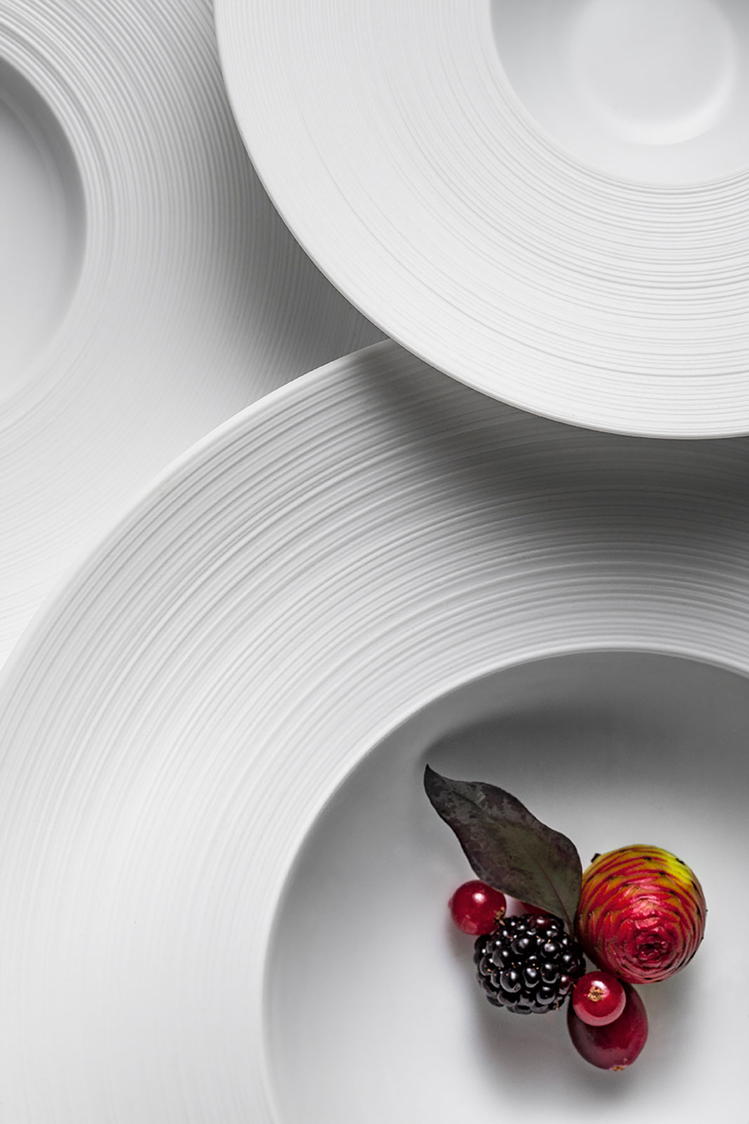 Detailaufnahme von oben. Auf dem Hémisphère Satin white Suppenteller befinden sich rote Früchte. Das Schattenspiel zeigt, wie edel das matte Finish auf den Fahnen aussieht.