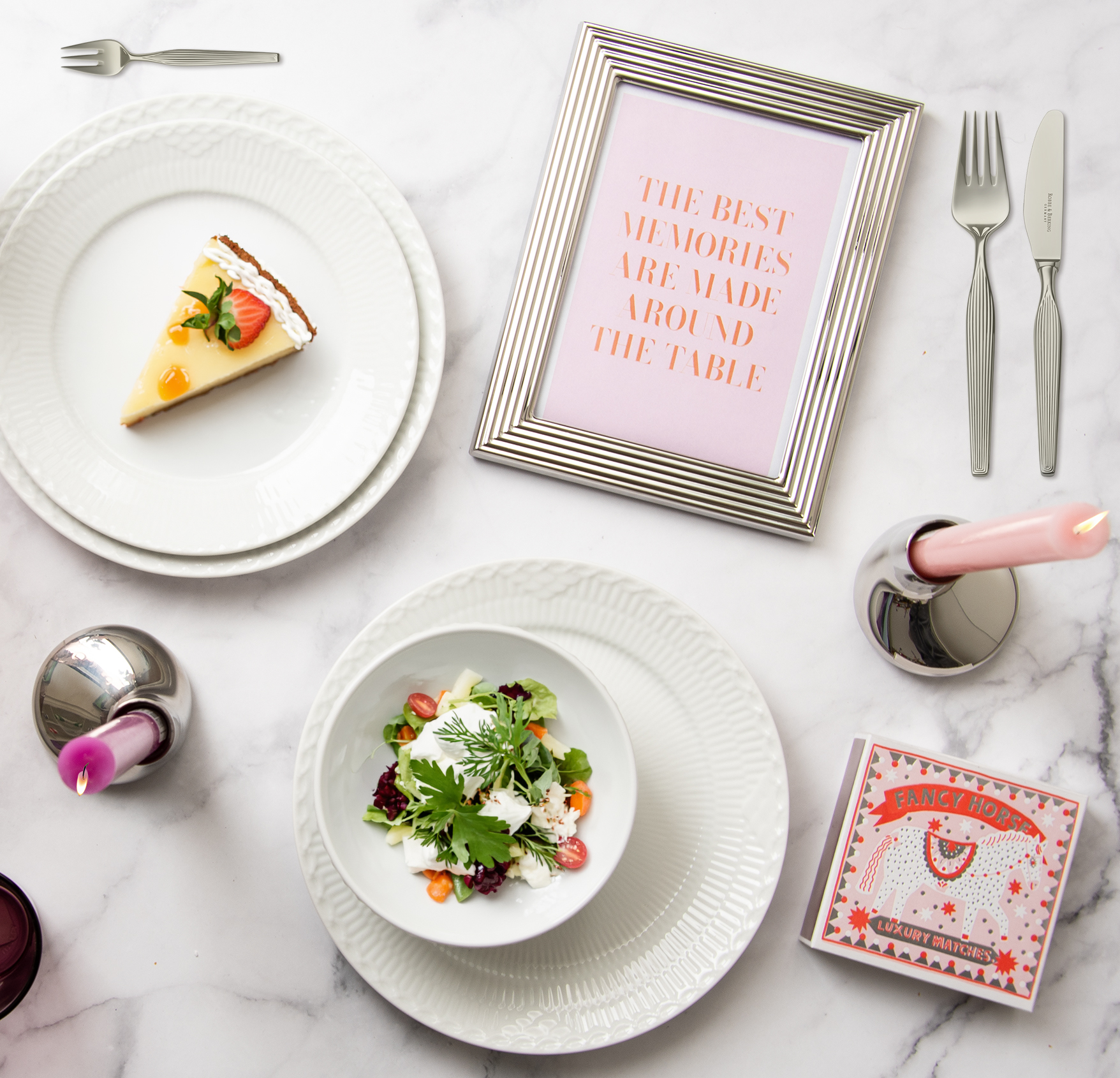 Ein gedeckter Tisch von oben fotografiert. Auf dem Tisch liegt inmitten von weißem Porzellan ein silberner Bilderrahmen. Im Rahmen ist ein Bild mit der Aufschrift: "The best memories are made around the table".