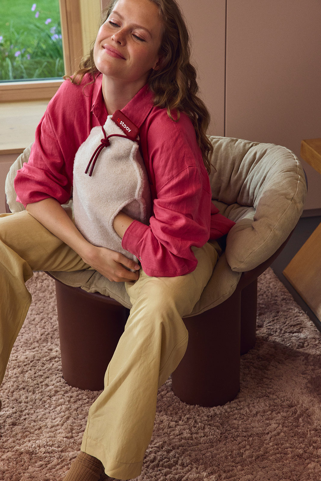 Eine lachende Frau im pinken Pullover hält sich die Homey XL Wärmflasche Teddy Off-White gegen den Bauch.