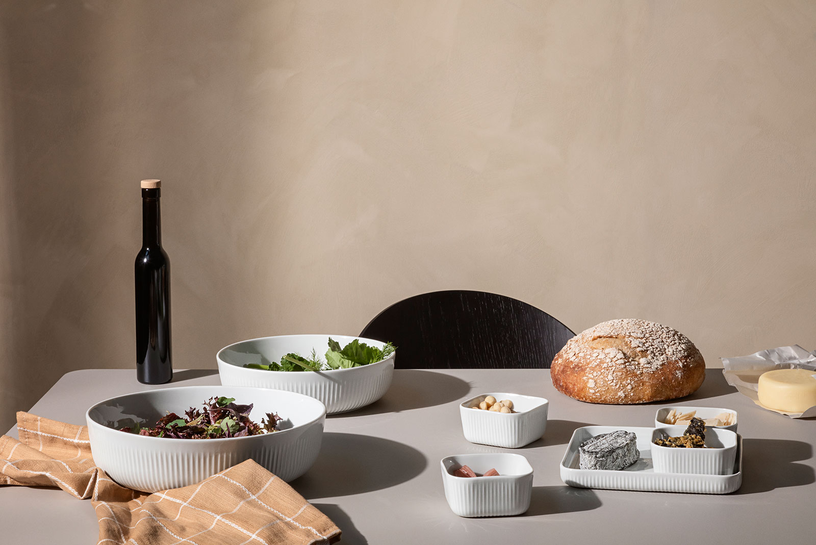 Auf einem Tisch ist Legio Nova Geschirr eingedeckt für eine gesunde Mahlzeit. In den Schalen befindet sich grüner Blattsalat und ein Laib Brot wartet darauf, angeschnitten zu werden.