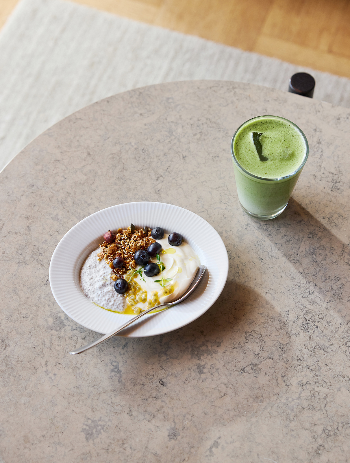 Ein runder Tisch, auf dem ein tiefer Eva Trio Teller mit Müsli sowie ein Glas mit grünem Smoothie stehen.