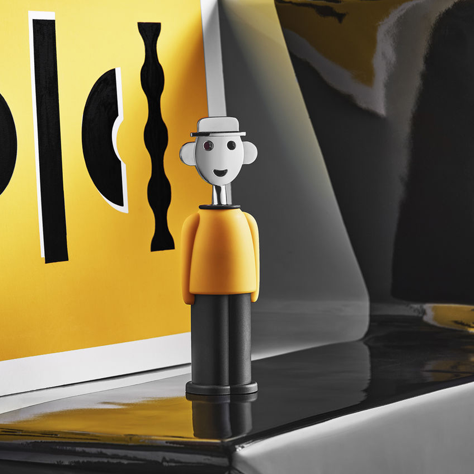Alessi Alessandro M. Korkenzieher in gelb-schwarz von Alessandro Mendini auf einem gedeckten Tisch.