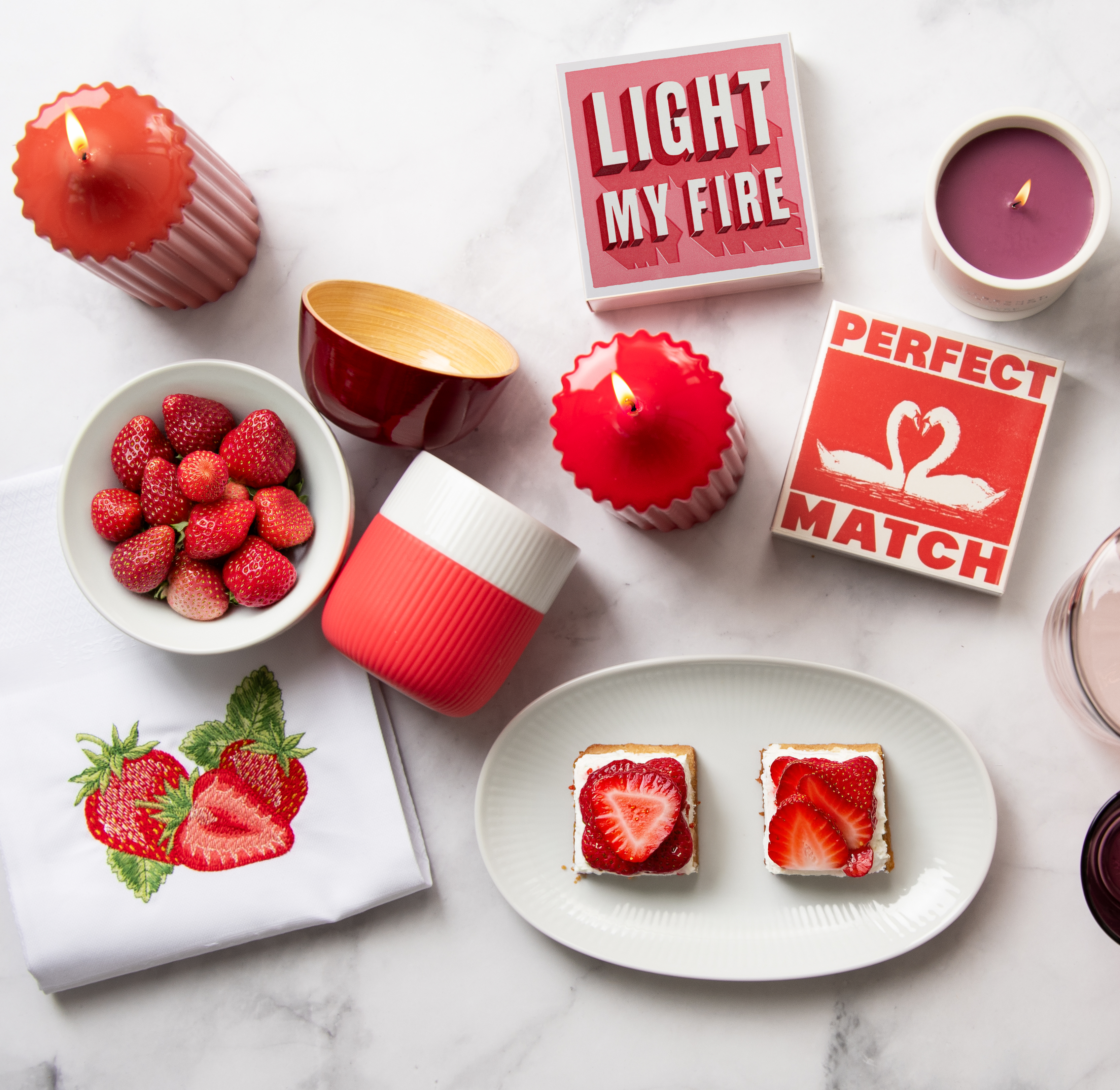 Ein gedeckter Marmortisch von oben fotografiert. Auf dem Tisch stehen vorwiegend rosa-rote Tischaccessoires sowie die Archivist Streichholzschachtel mit dem Print: "Perfect Match".