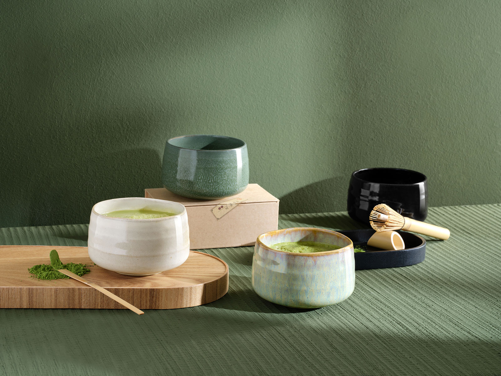 Vor einem grünen Hintergrund stehen vier Moribana Matcha Schalen in verschiedenen Farben.