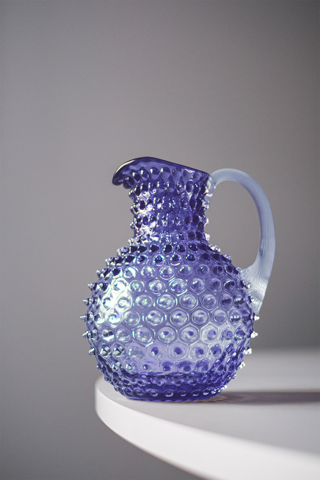 Der Paris Hobnail Krug Lavender steht vor grauem Hintergrund auf einem Tisch.