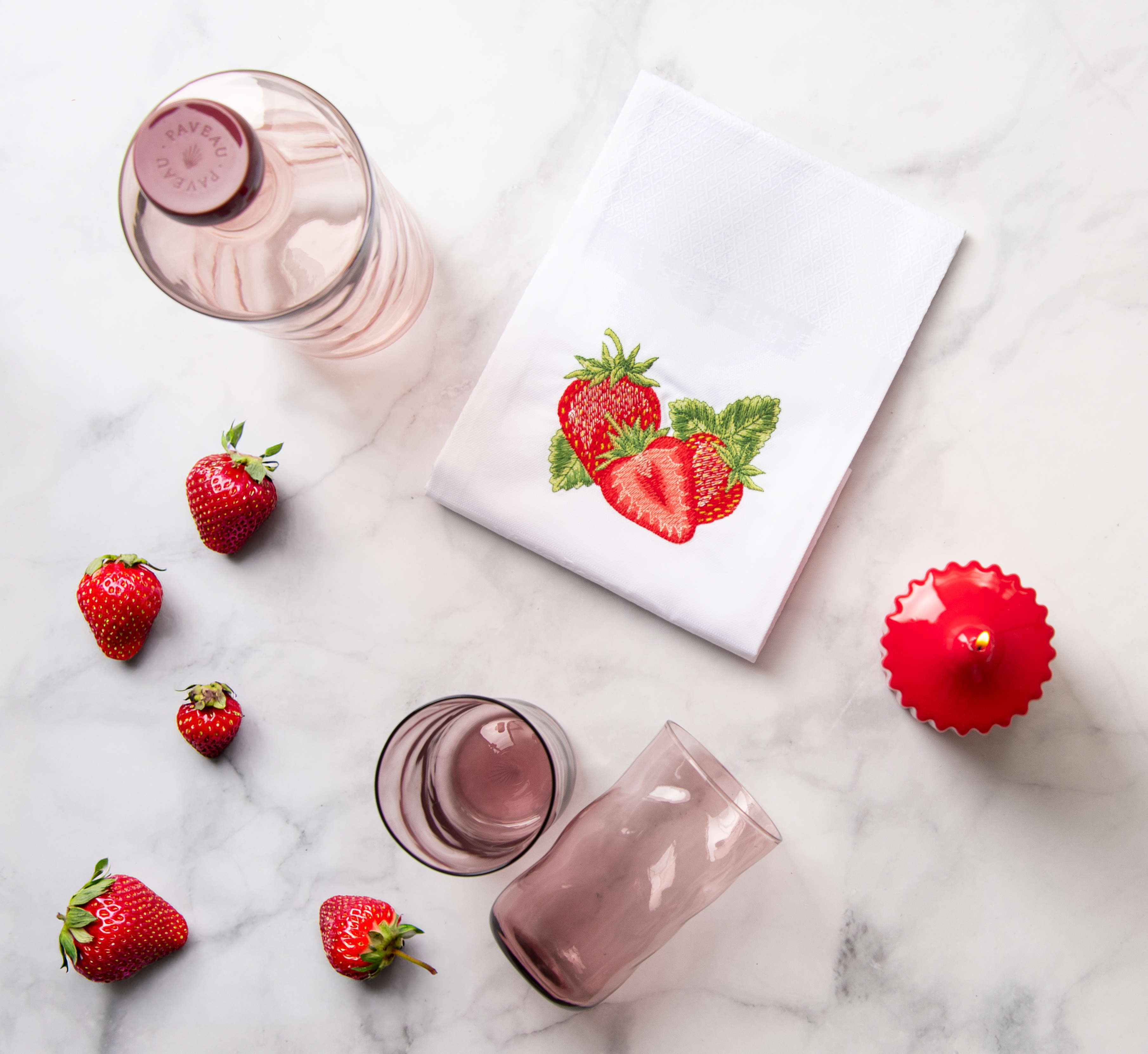 Ein gedeckter Marmortisch von oben fotografiert. Auf dem Tisch stehen rote Tischaccessoieres sowie das Vista Portuguese Geschirrtuch mit dem Motiv Erdbeeren.