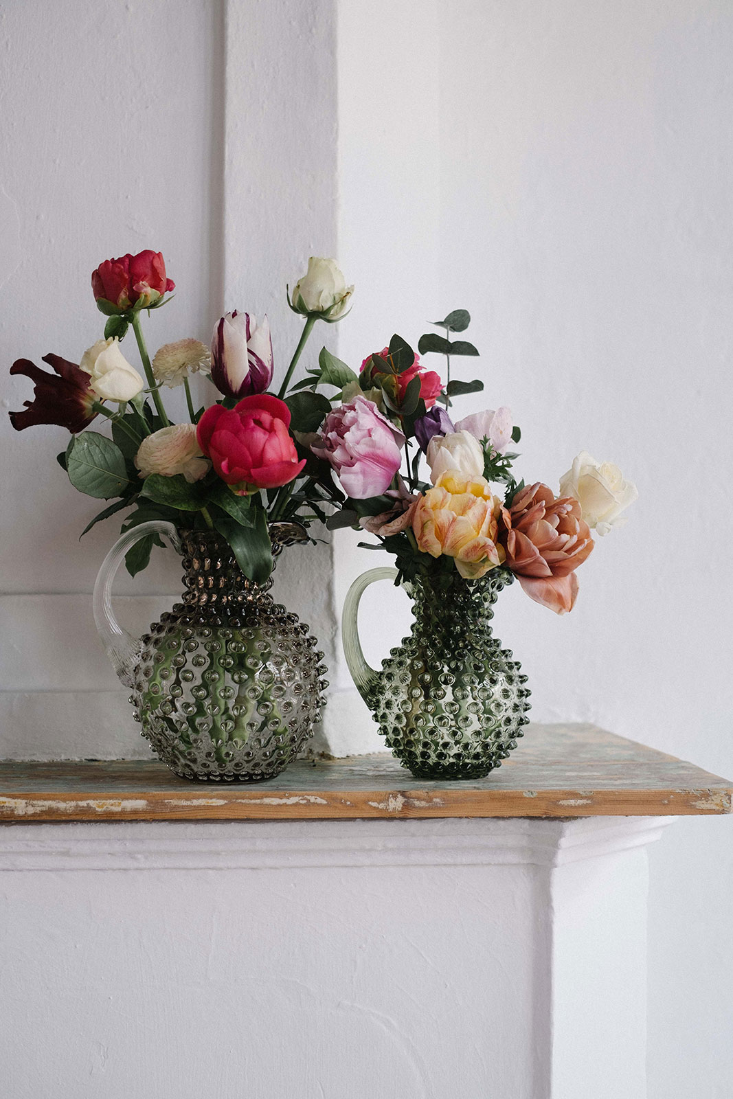 Auf einem hölzernen Kaminsims stehen zwei Paris Hobnail Krüge, gefüllt mit lebhaften Blumenarrangements.