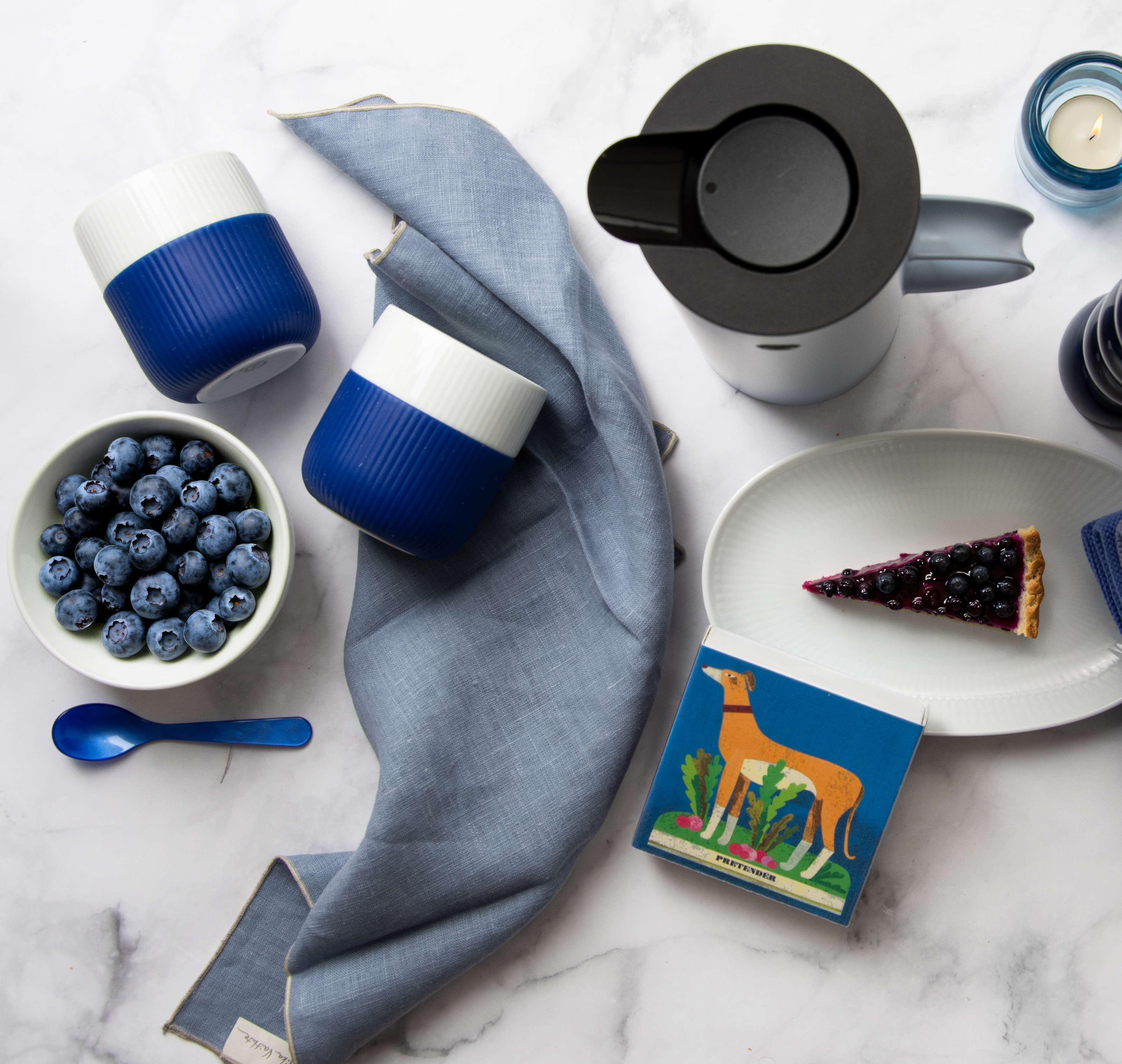 Ein gedeckter Marmortisch von oben fotografiert. Auf dem Tisch stehen blau-weiße Tischaccessoieres sowie die Erika Vaitkute Leinen-Serviette in taubenblau.