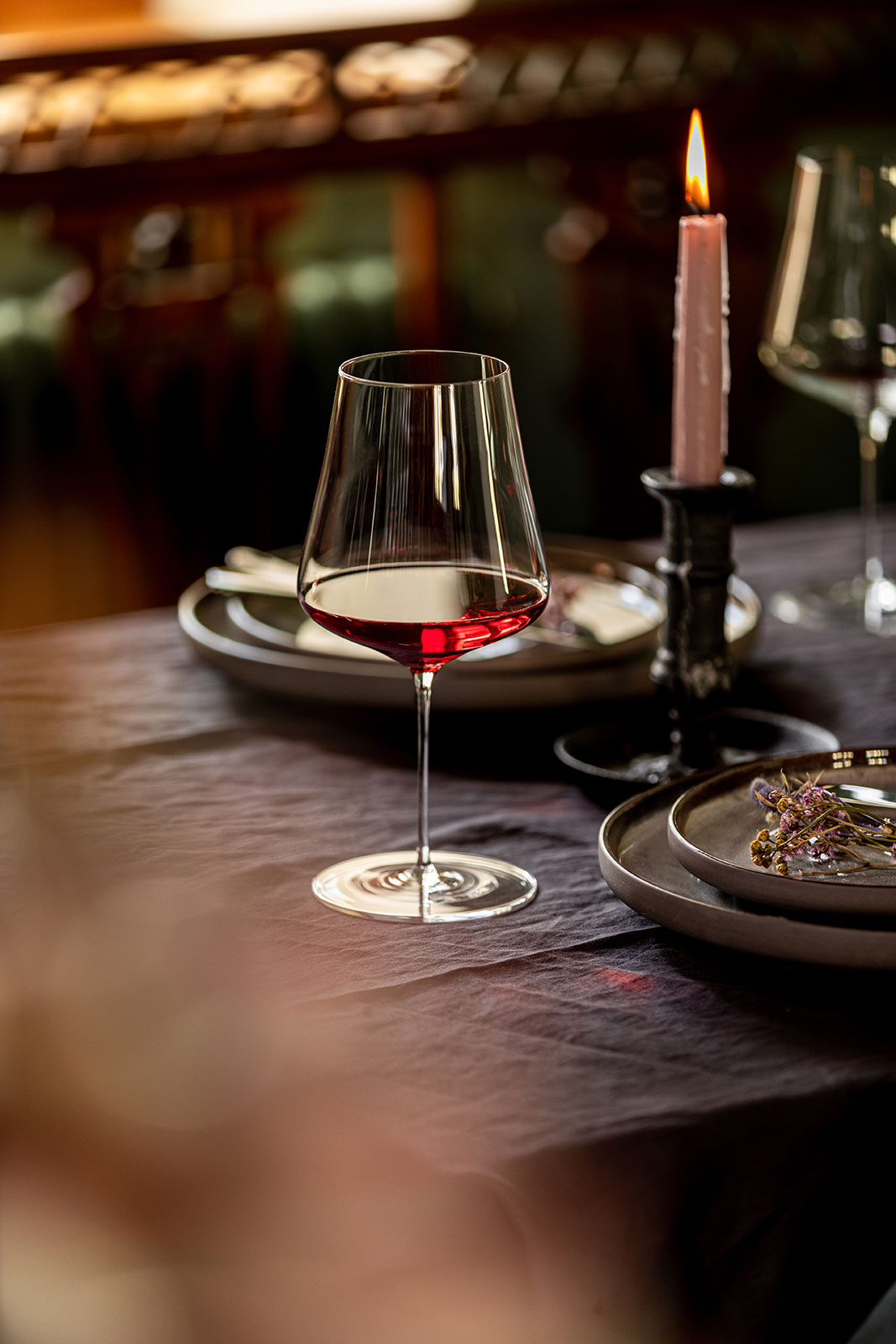 Auf einem edel gedeckten Tisch steht ein DUO Burgunder Weinglas mit dunkelrot leuchtendem Rotwein darin.